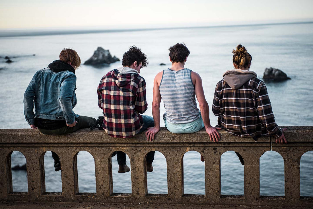 Four people enjoying the view of the ocean while sitting on a railing.