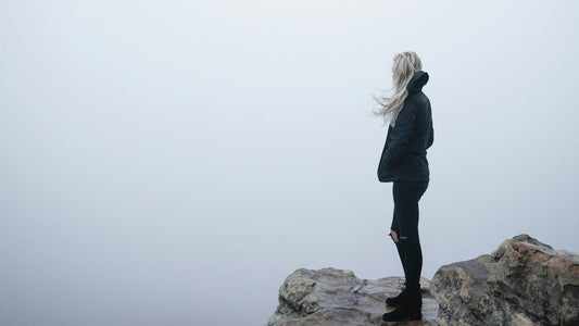 woman standing on cliff looking at cloudy sky